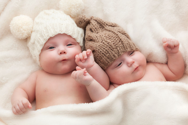 戴着羊毛绒球帽双胞胎姐妹的婴儿躺在一起