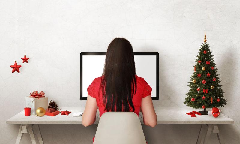 女人使用电脑的桌子上的圣诞树和礼品