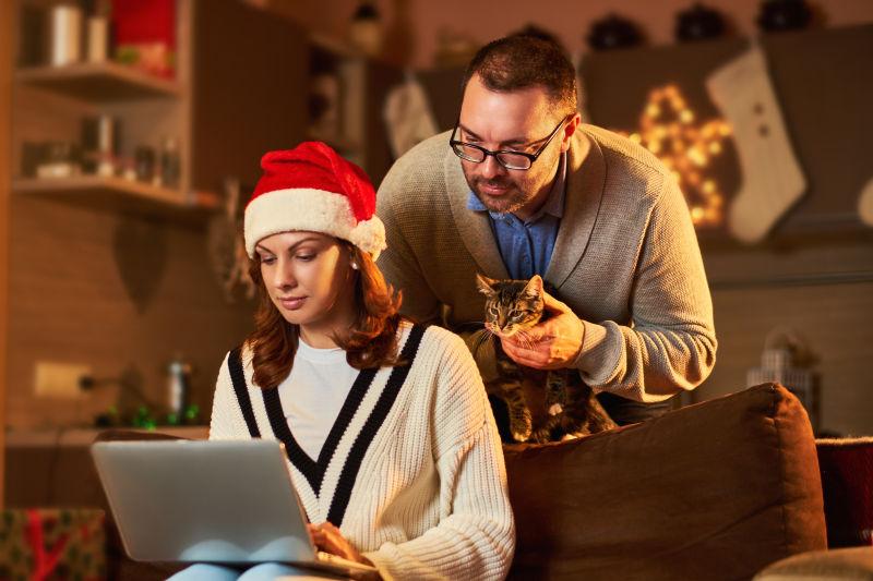 戴着圣诞帽的美女与男人看着笔记本电脑