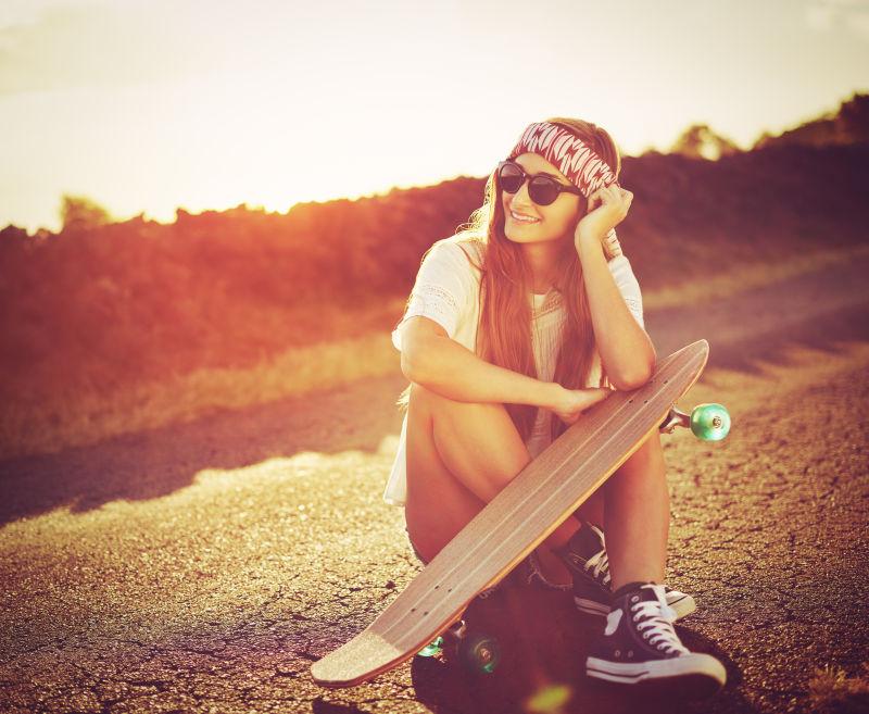 夕阳下拿着滑板的美丽姑娘