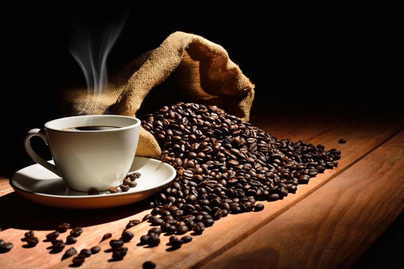 黑色背景下木桌上的咖啡豆和冒着热气的咖啡