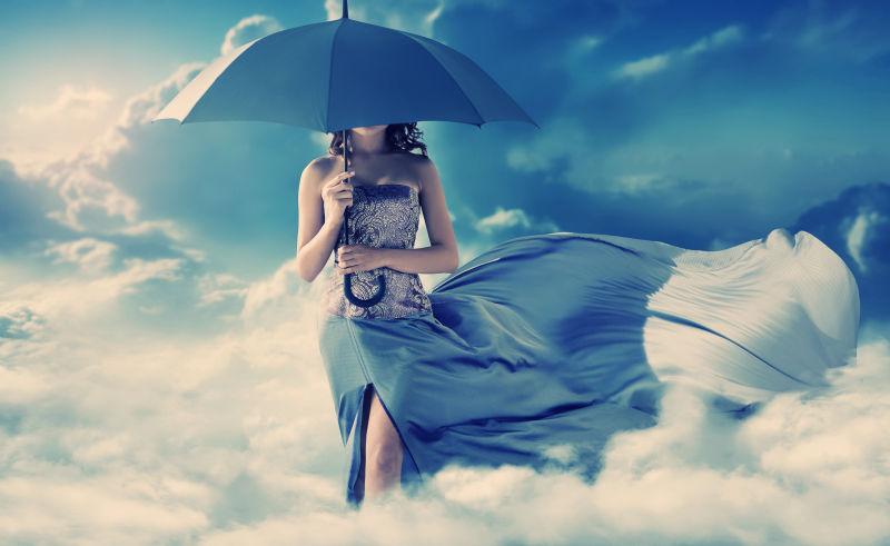 蓝天白云背景上穿着蓝色连衣裙撑着雨伞坐在云上的美女