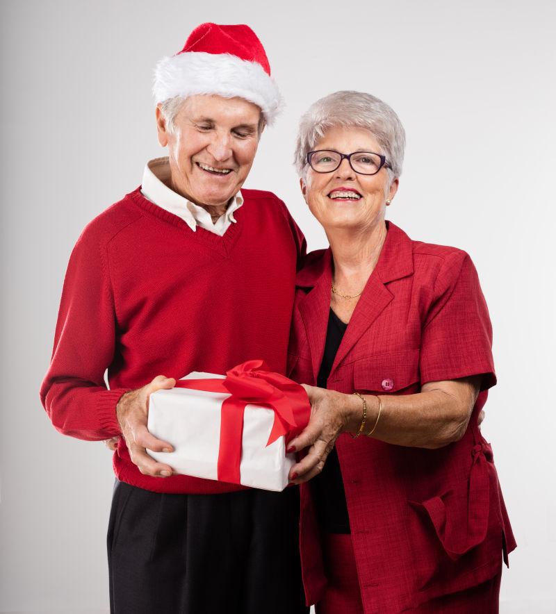 灰色背景上的拿着圣诞礼物的老年夫妇