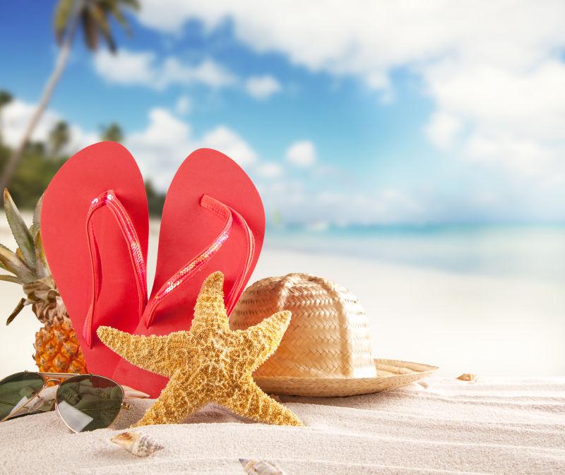 夏日沙滩上的海星草帽与红色拖鞋
