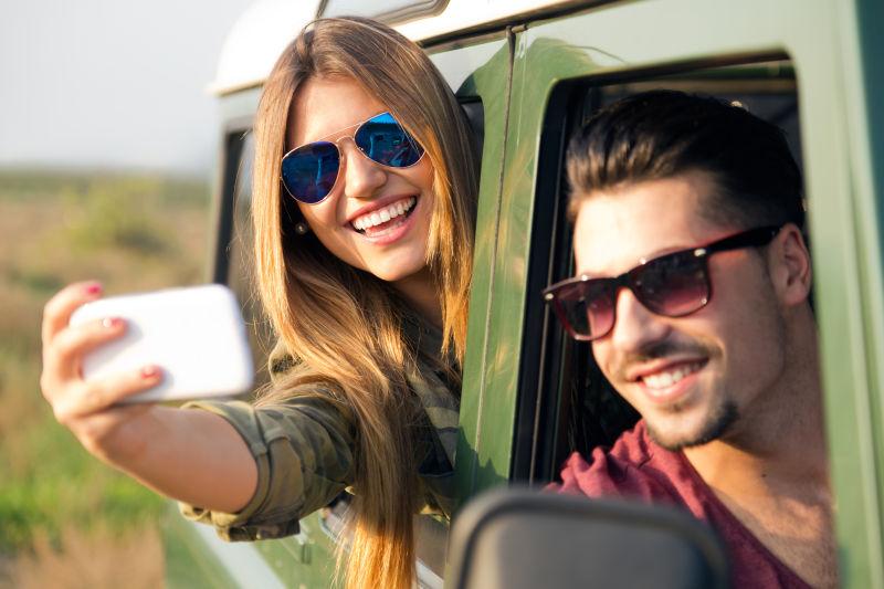 漂亮的夫妇采取selfie与车内智能手机自拍