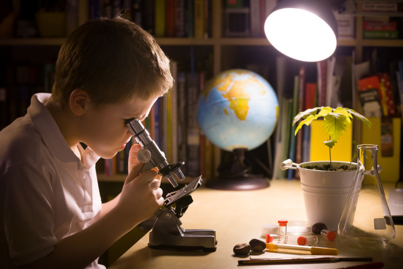 书桌上使用显微镜研究样品的年轻学生