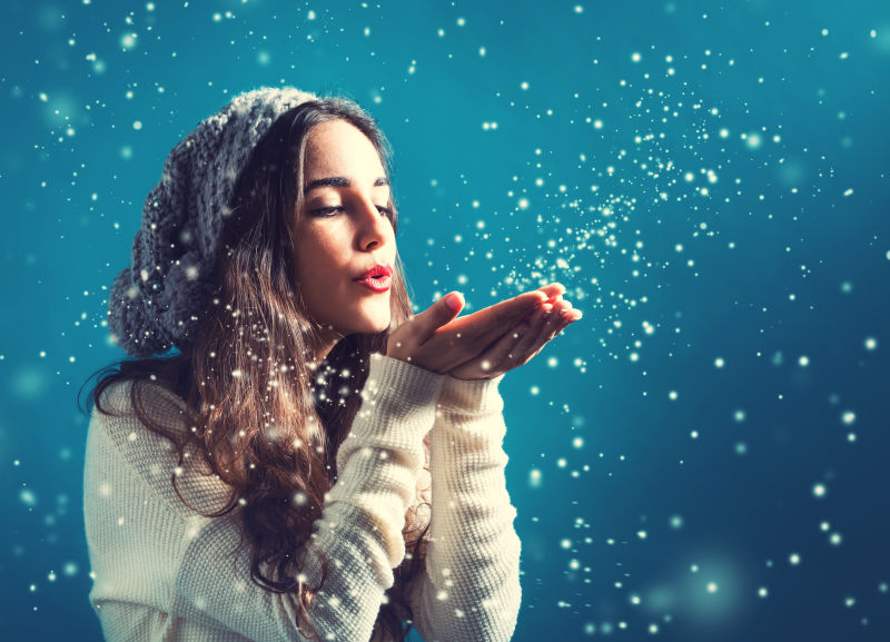 快乐的年轻女子穿着冬装吹着雪