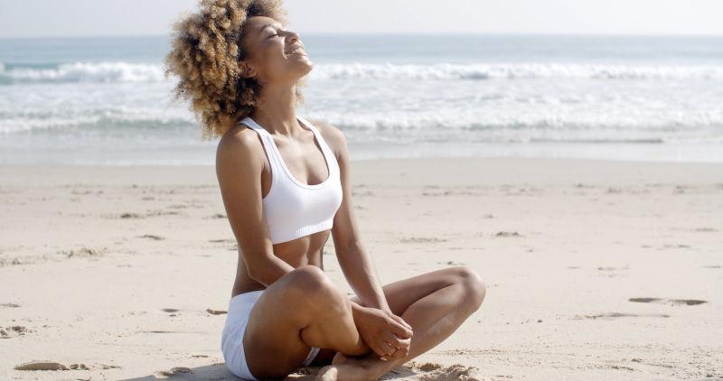 坐在夏日的海滩上练习瑜伽冥想的年轻女人