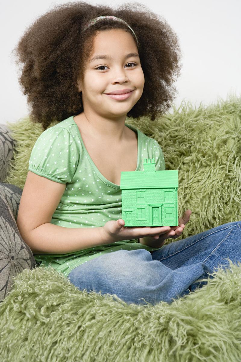 沙发上的小女孩拿着绿色风房屋模型