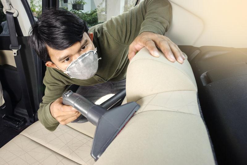 戴口罩的男人用吸尘器清洗他的汽车