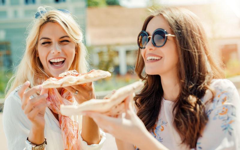 两个年轻妇女在户外吃披萨的肖像
