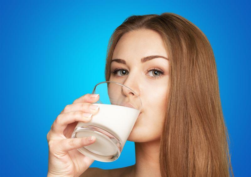 在蓝色背景下正在喝牛奶的年轻女子