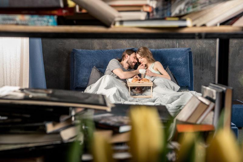 透过书架看年轻夫妇在床上吃早餐