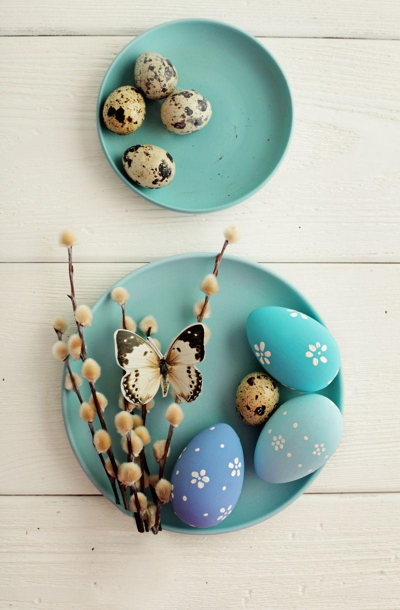 白色桌上蓝色盘子里的蓝色复活节彩蛋和鹌鹑蛋