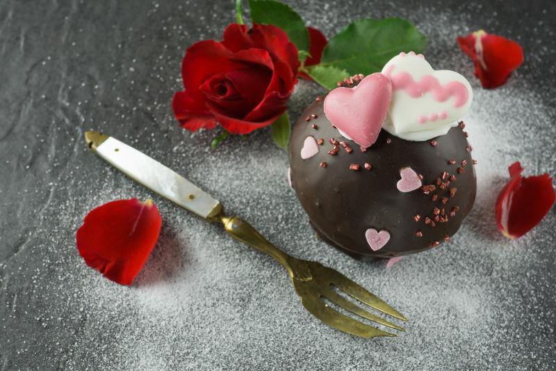 糖粉背景中的巧克力甜点叉子和红色玫瑰