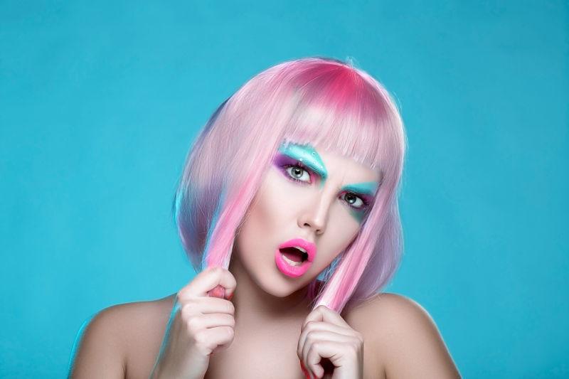 浅蓝色背景下画着创意妆容的扯着自己的粉色短发的美女