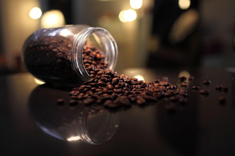 黑色桌上的玻璃瓶里撒落出来的咖啡豆