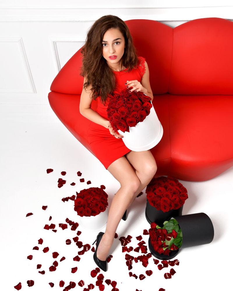 年轻美女抱着玫瑰花坐在红唇沙发上