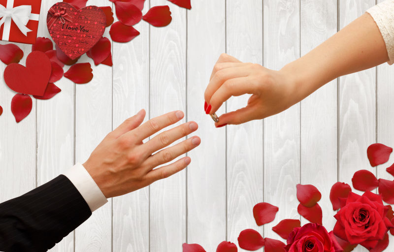 有玫瑰花花瓣背景的女人把订婚戒指放在男人手上