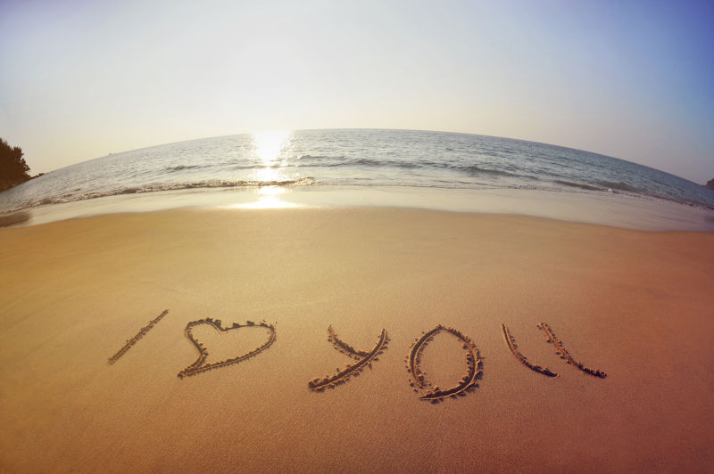 铭刻“我爱你”的心写在沙滩上的大海和夕阳的背景