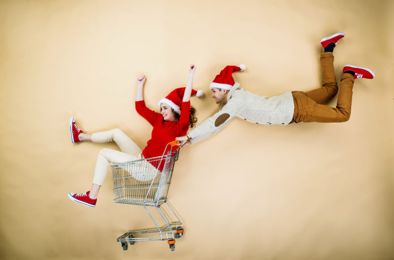 带着圣诞帽的年轻情侣推着购物车去购物