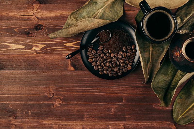 棕色木桌背景上干燥的叶子和黑咖啡与咖啡豆