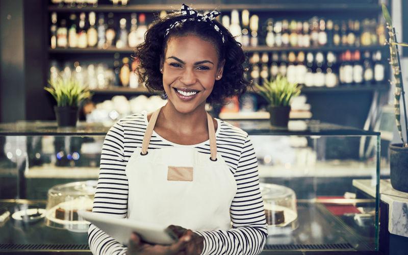 微笑的企业家站在她的咖啡馆里用数字平板电脑