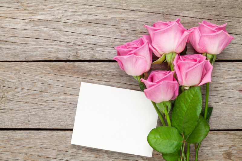 粉红玫瑰花束和空白贺卡在木桌上