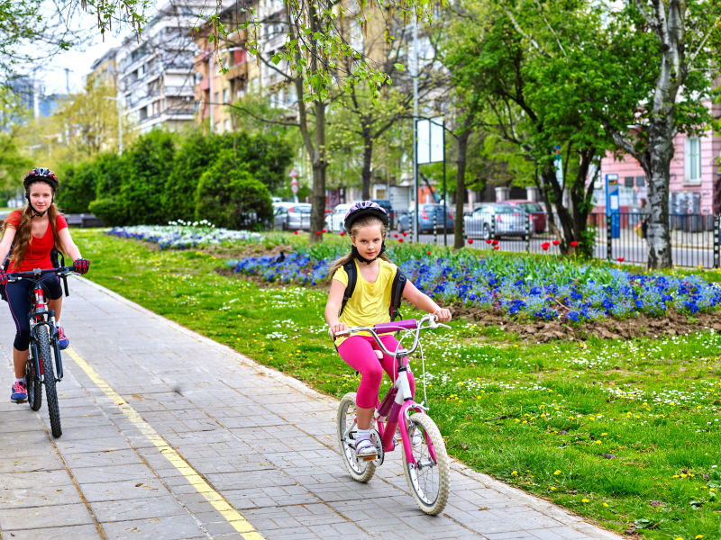 骑自行车的女孩女孩们戴着自行车头盔背着帆布包骑着自行车女童在黄色自行车道上骑车自行车共享计划节省金钱和时间孩子们争先恐后
