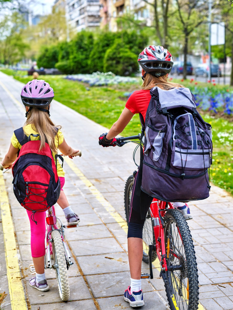 骑自行车的女孩女孩们戴着自行车头盔背着帆布包骑着自行车女童在黄色自行车道上骑车自行车共享计划节省了城市街道的金钱和时间后视图