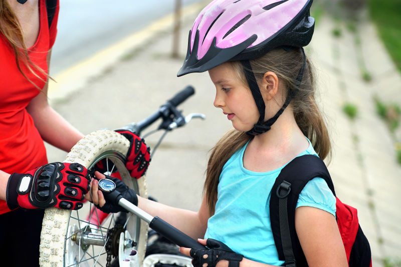 骑自行车的女孩一家人戴着自行车头盔手上装有自行车打气筒女孩给自行车轮胎打气背景是道路和人行道
