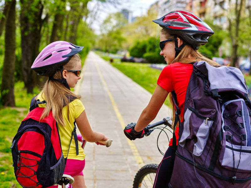 骑自行车的女孩女孩们戴着自行车头盔背着帆布包骑着自行车女童在黄色自行车道上骑车自行车共享计划后视图我是骑自行车的女孩
