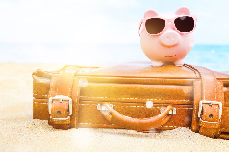 粉红色的小猪存钱罐-戴着太阳镜-皮包-背景是海滩-节余度假概念