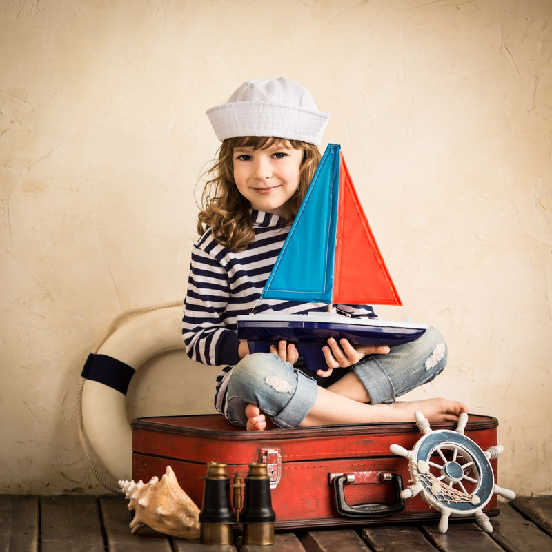 快乐孩子在室内玩玩具帆船-旅行与冒险概念