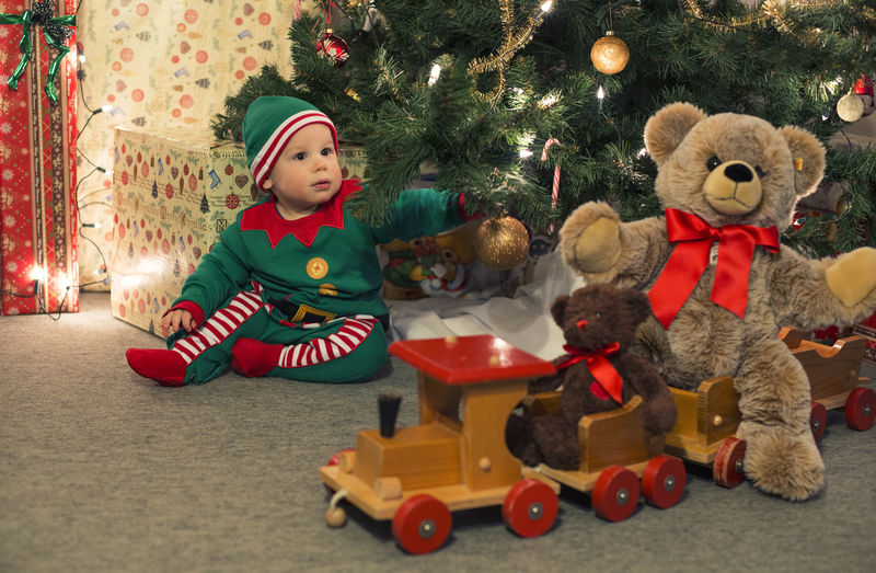 穿着精灵服装的婴儿在圣诞树下玩旧木火车和软玩具熊-复古