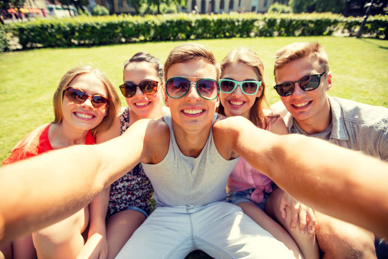 友谊休闲夏天科技和人的概念——公园里一群微笑的朋友用智能手机相机或平板电脑自拍