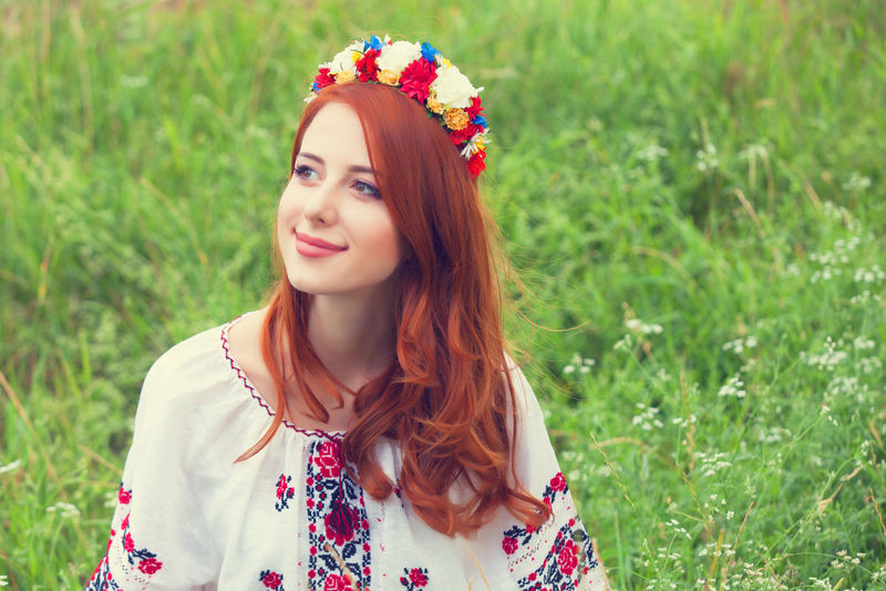在绿草上穿着乌克兰民族服装的红头发女孩