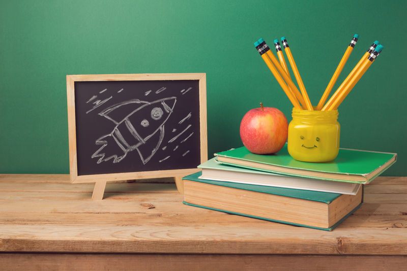 回到学校背景书铅笔放在emoji罐子里苹果黑板和木制桌子上的火箭草图