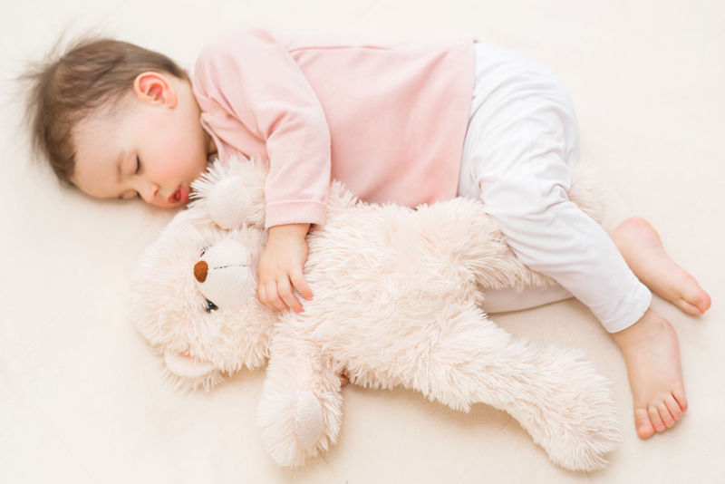 睡在床上的漂亮的幼儿女孩和毛绒玩具熊
