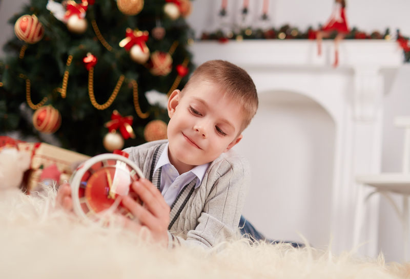 可爱的小男孩躺在背景上-手里拿着圣诞装饰品和红色的时钟