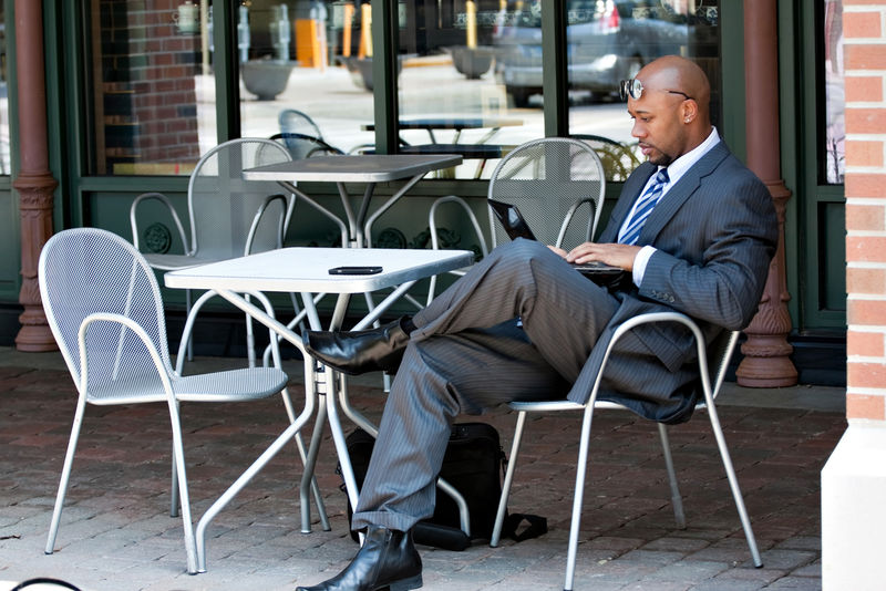 一个30出头的非裔美国人-坐在室外的咖啡桌旁-用笔记本电脑或上网本电脑