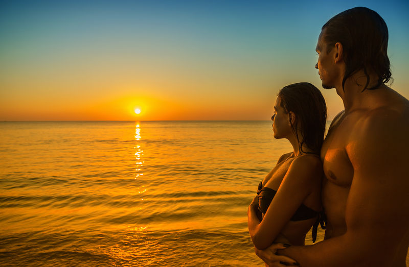 快乐的年轻夫妇在热带海滩上遇见日落