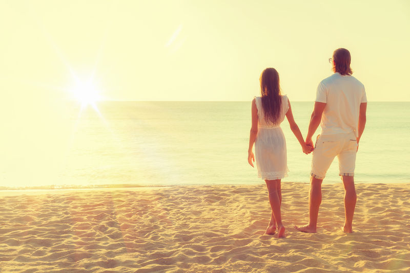 这对幸福的年轻夫妇在热带海滩上遇见了日落-海滩上身躯丰满的情侣-后视图