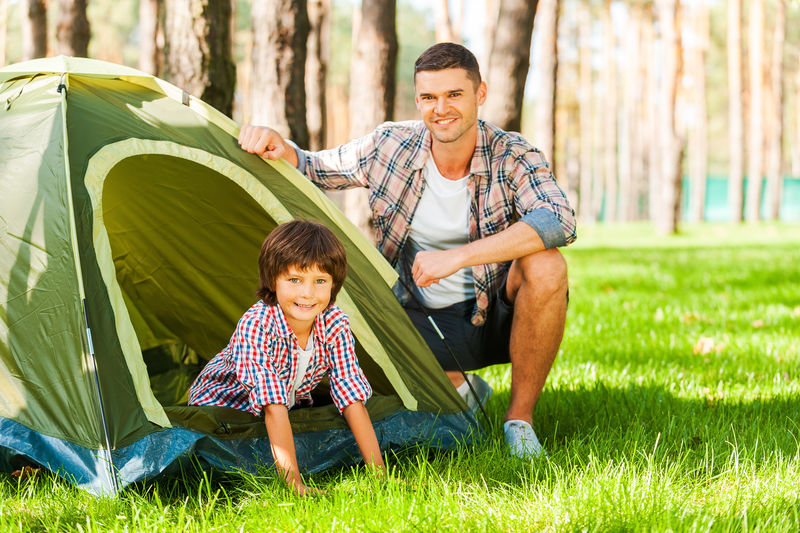户外探险-快乐的父子坐在帐篷旁-在森林里露营