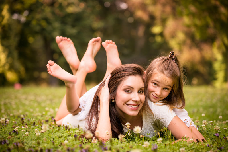 美丽快乐的母亲和她的女孩躺在草地上-大自然中的户外