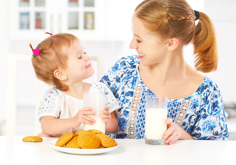 早餐时快乐的家庭母亲和女儿小女儿：牛奶饼干