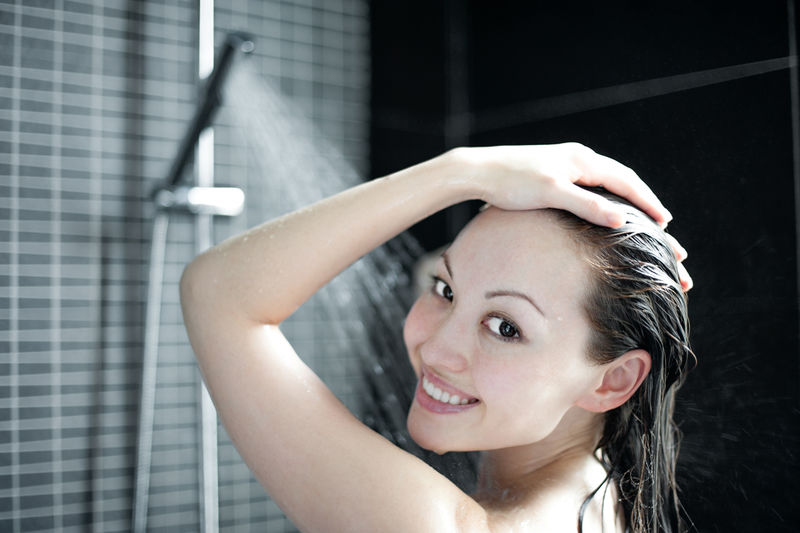 迷人的混合亚洲女性在淋浴时微笑看着相机