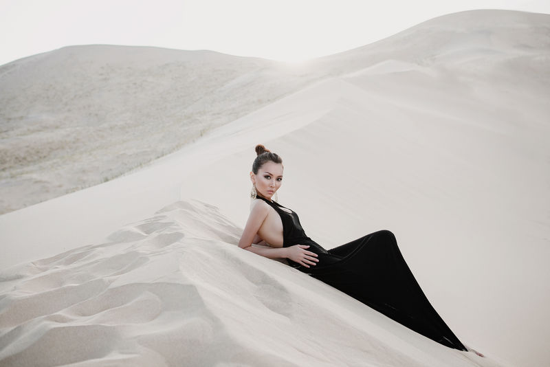 在沙漠的沙丘上穿着黑色连衣裙的美丽性感的亚洲女人