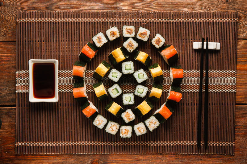 日本美食艺术。美味的Uramaki卷轴套装，彩色圆形寿司点缀在棕色草席上，平放。豪华餐厅菜单照片。