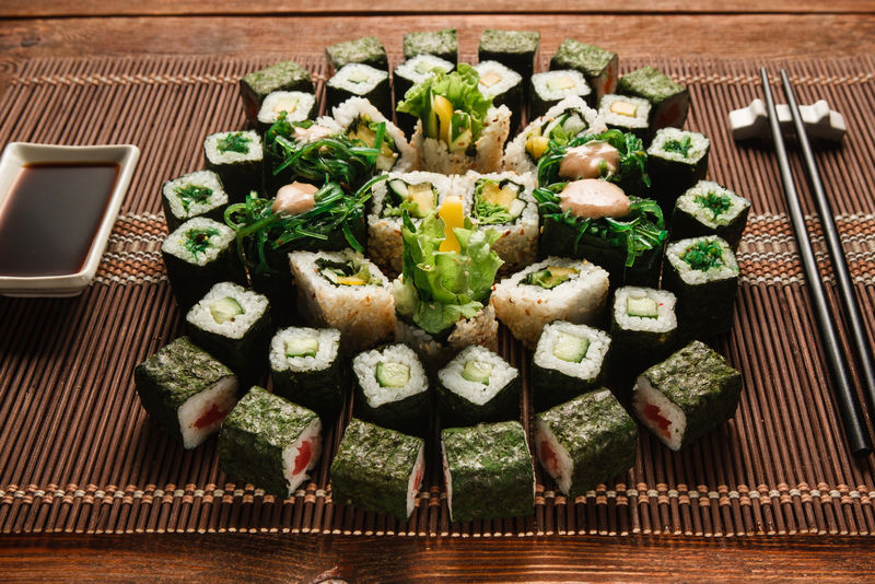 美食艺术，日本传统美食。绿色寿司卷的圆形装饰，放在棕色草席上，特写。日本海鲜，烹饪杰作。